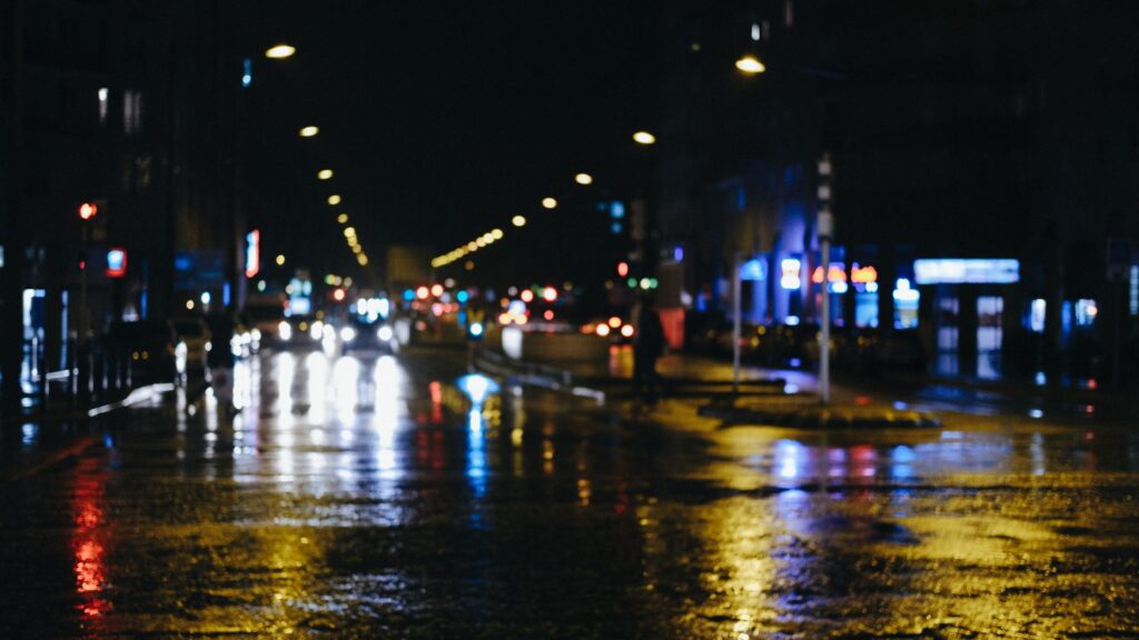 Blurred streetlights and car headlights on a dark road, representing the challenges of night vision.